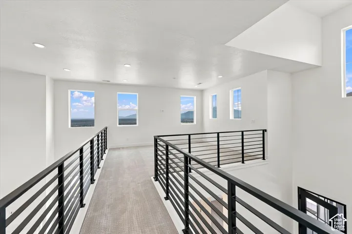 Open-concept walkway featuring metal horizontal-rail balustrades, recessed ceiling lighting, wall-to-wall carpeting, and multiple windows with mountain topography exposure