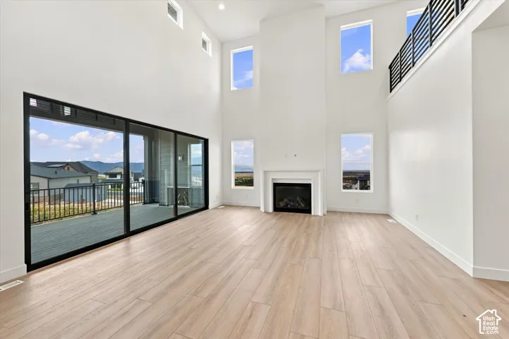 Double-height living area featuring wood-finish flooring, a full-height fireplace, multi-panel sliding glass doors, and a metal-railing mezzanine