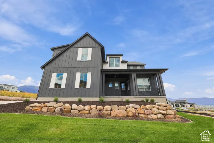 Modern two-story exterior featuring vertical board-and-batten siding, contrasting white shutters, a covered porch, and natural stone retaining walls