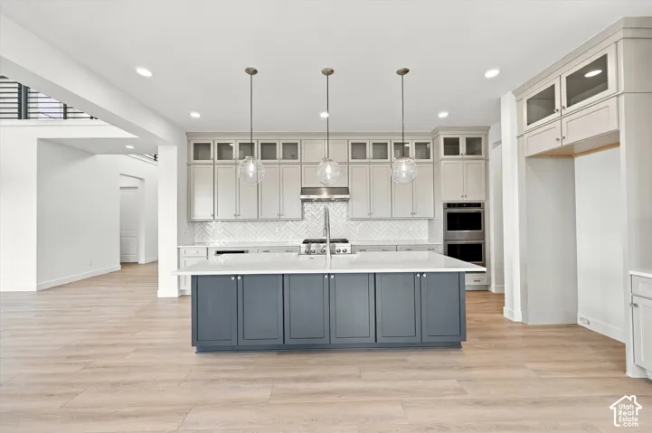 Kitchen featuring a central island with a solid-surface countertop, ceiling-height cabinetry, herringbone-patterned tile backsplash, built-in double wall ovens, and recessed lighting