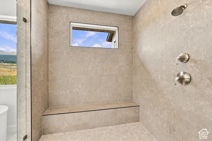 Walk-in shower featuring floor-to-ceiling stone-finish tile, a built-in stone bench, a horizontal transom window, a frameless glass door, and brushed-finish fixtures