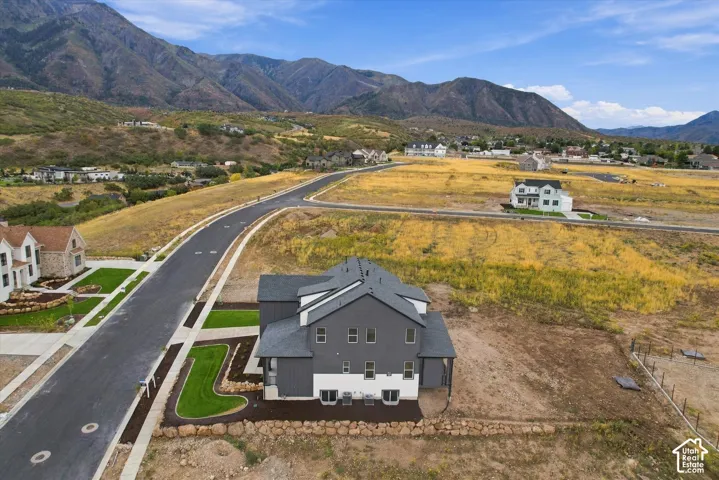 Aerial perspective of a two-story residence featuring a dark gray and white exterior finish, dark-toned roof shingles, mountain backdrop, and manicured turf borders