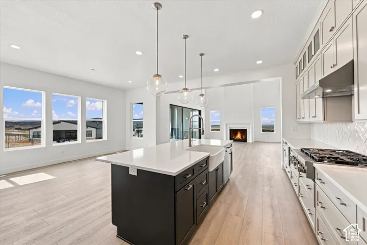 Kitchen featuring a central island with a farmhouse-style sink, quartz countertops, wood-finish flooring, glass pendant lighting, and built-in cabinetry with a herringbone-patterned tile backsplash