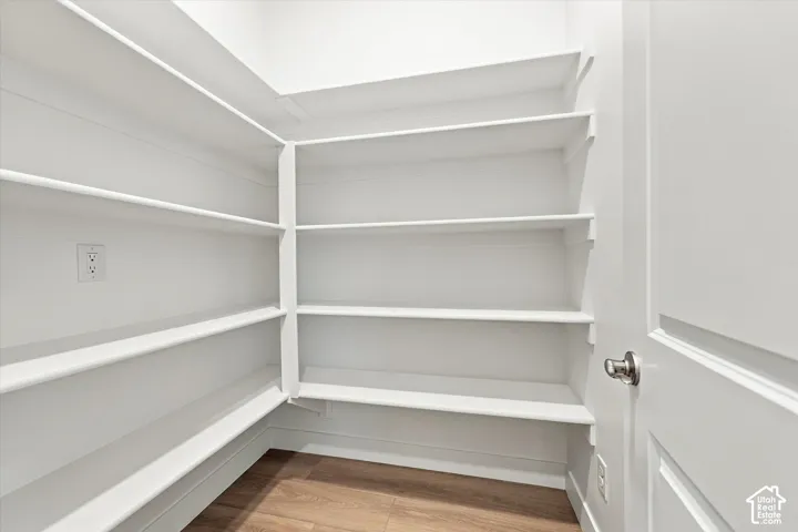 Walk-in storage space featuring custom white multi-tier shelving and wood-finish flooring