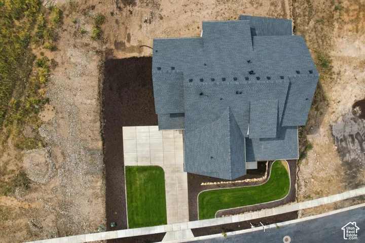 Aerial perspective featuring a multi-gabled architectural roofline, a concrete driveway, a manicured lawn, and defined landscape beds