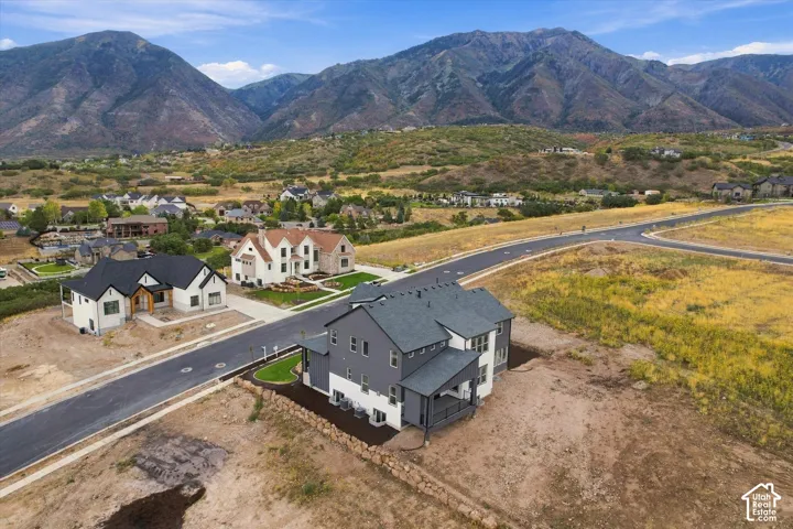 Multi-story residence featuring a dark-toned composite shingle roof, exterior siding in contrasting neutral palettes, covered rear patio, and mountainous backdrop