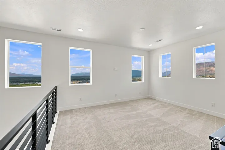 Neutral-toned carpeted flooring, recessed lighting, matte black metal railing, and expansive windows showcasing mountain scenery