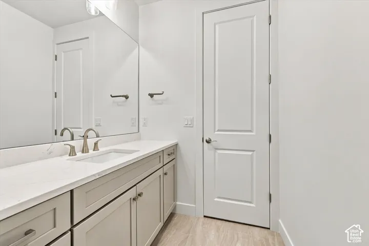 Shaker-style cabinetry with neutral finish, light-toned stone countertop, undermount sink with metallic hardware, full-width wall mirror, and two-panel interior door