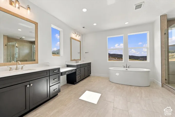Double vanity with dark cabinetry, light-toned stone countertops, undermount sinks, and framed mirrors, complemented by a freestanding soaking tub, ceramic tile flooring, and a glass-enclosed shower