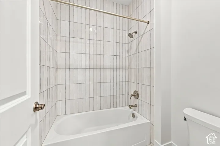 Bathtub enclosure featuring floor-to-ceiling vertical ceramic tile surround, brushed nickel shower fixtures, and a metallic shower curtain rod