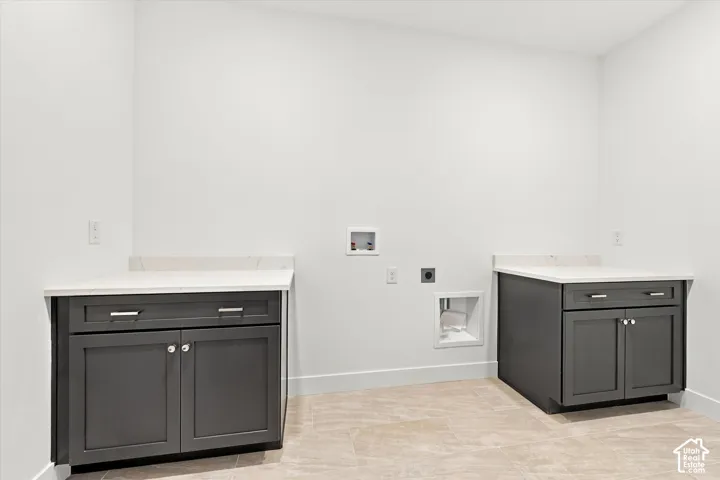 Dedicated utility area featuring dark grey shaker-style cabinetry, light-toned stone-finish countertops, and ceramic tile flooring