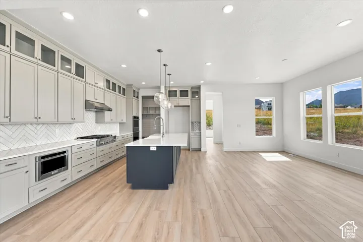 Kitchen featuring floor-to-ceiling cabinetry, a contrasting center island with quartz countertops, herringbone tile backsplash, and wood-finish flooring