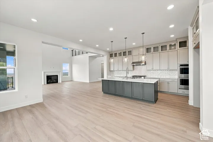 Kitchen featuring a center island, light-colored cabinetry with glass-front uppers, herringbone tile backsplash, and built-in stainless steel appliances, complemented by wood-finish flooring and recessed lighting
