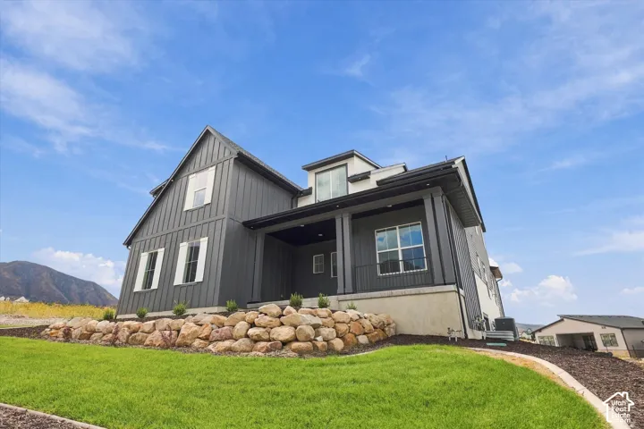 Modern vertical board-and-batten exterior with a covered front porch, stone retaining wall, and mountain backdrop