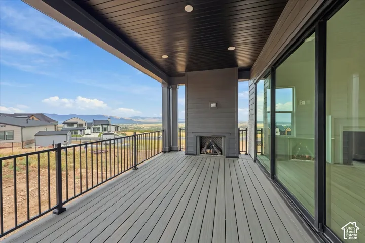 Covered patio featuring composite decking, a built-in outdoor fireplace, black metal railing, and floor-to-ceiling sliding glass doors
