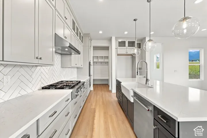 Kitchen featuring white shaker-style cabinetry, quartz countertops, a herringbone-patterned tile backsplash, a stainless steel gas range with a matching hood, and a farmhouse sink