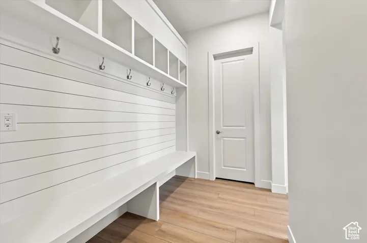 Built-in mudroom storage featuring white shiplap wall paneling, integrated upper cubbies, fixed wall hooks, and a bench with wood-finish flooring