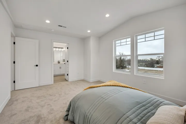 Bedroom with recessed lighting, vaulted ceiling, light colored carpet, and connected bathroom