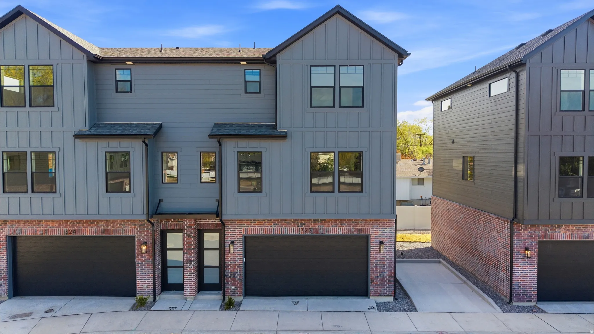 View of front facade featuring board and batten siding, an attached garage, driveway, and brick siding