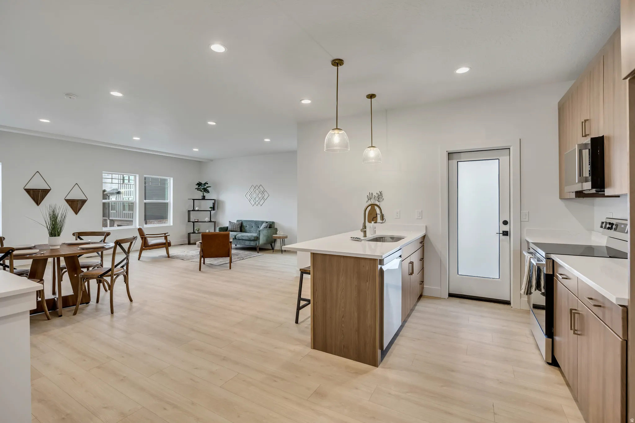 Kitchen featuring stainless steel appliances, a kitchen bar, a peninsula, decorative light fixtures, and light wood-style floors