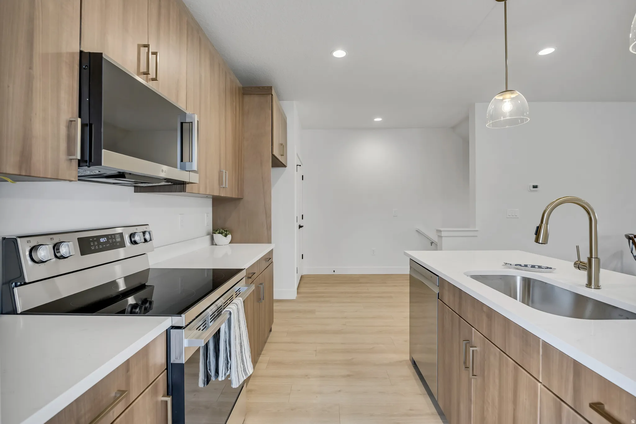 Kitchen featuring stainless steel appliances, light wood finished floors, decorative light fixtures, light stone counters, and modern cabinets