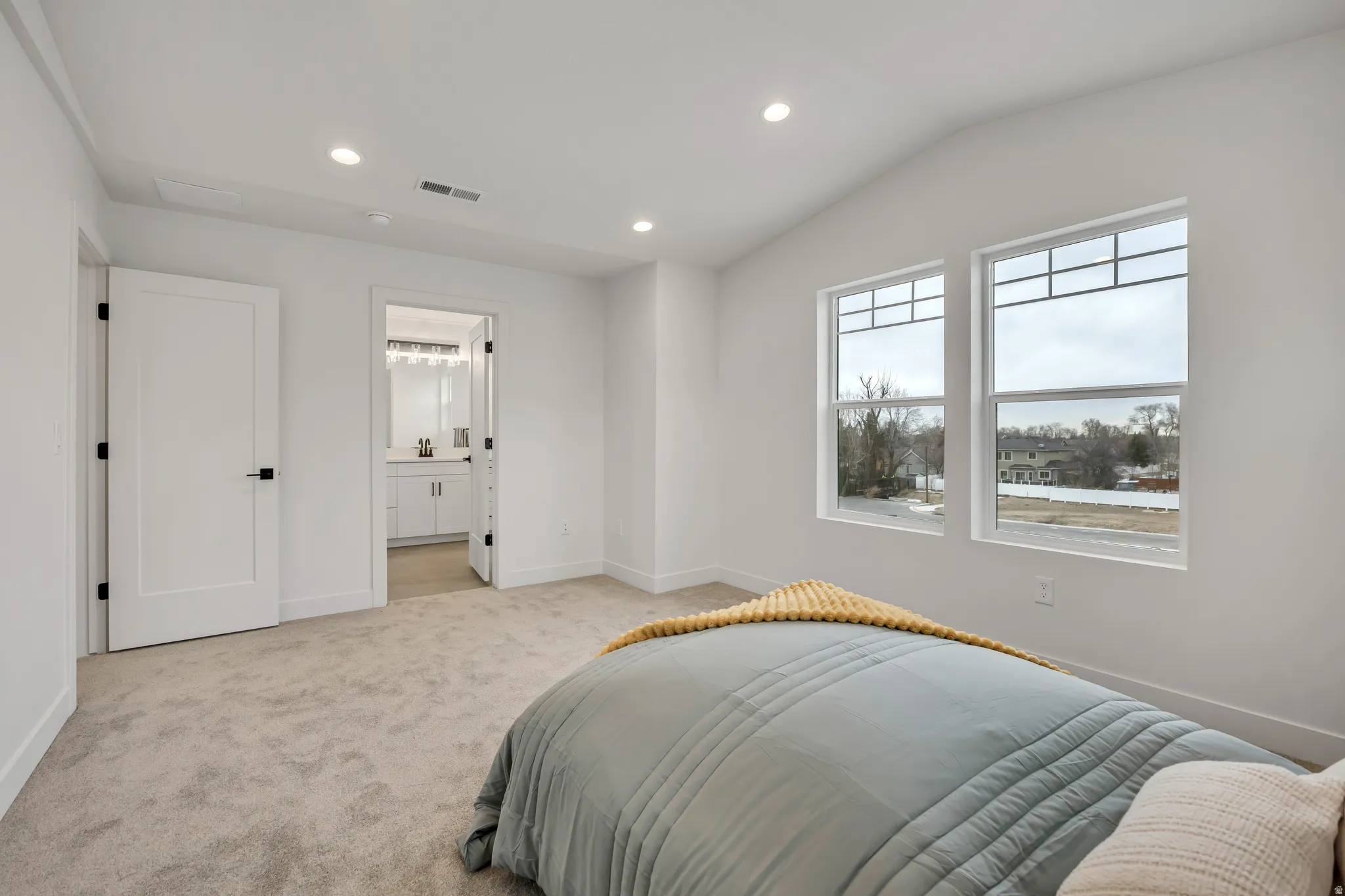 Bedroom with recessed lighting, vaulted ceiling, light colored carpet, and connected bathroom