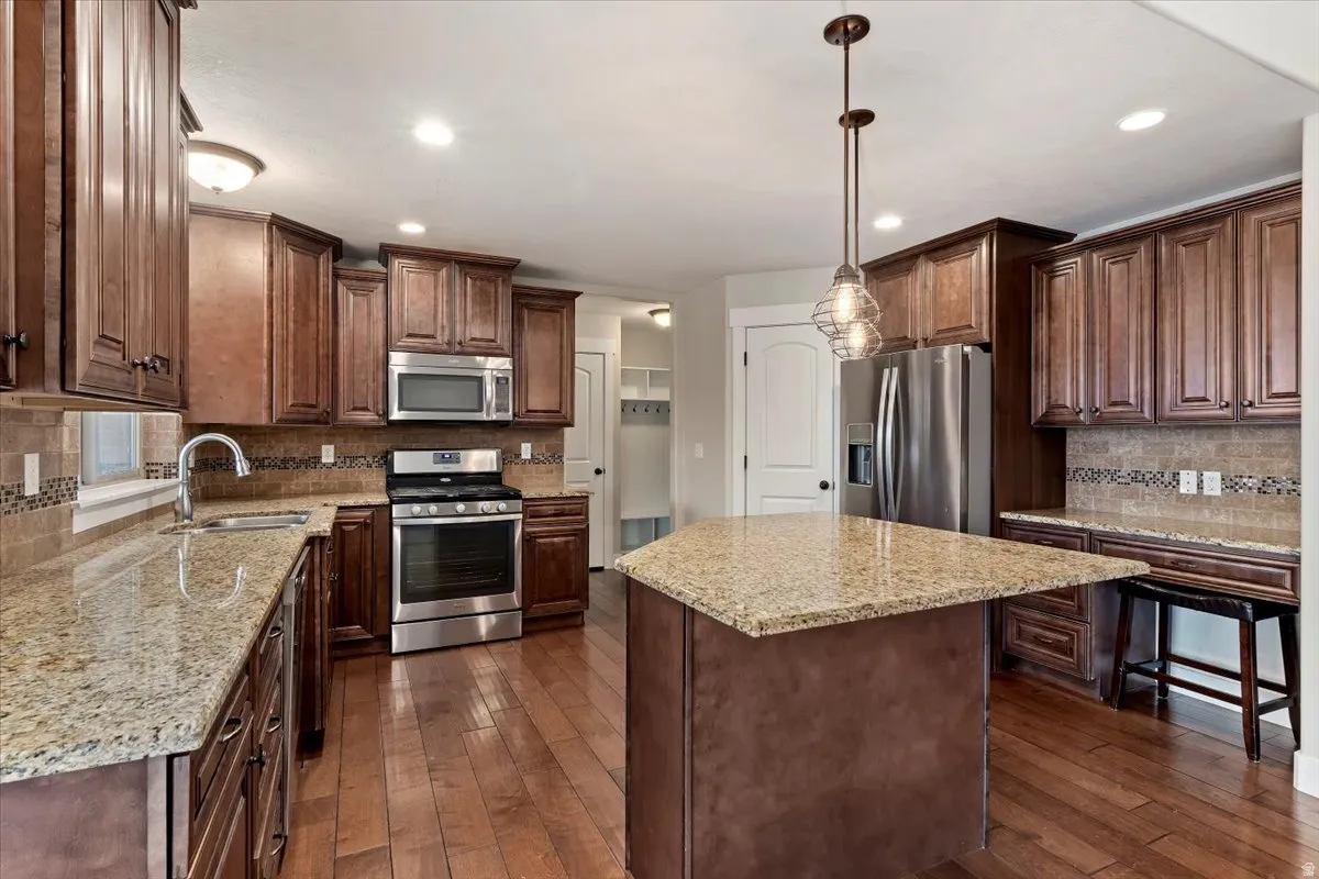 Kitchen featuring tasteful backsplash, stainless steel appliances, pendant lighting, and dark wood-type flooring