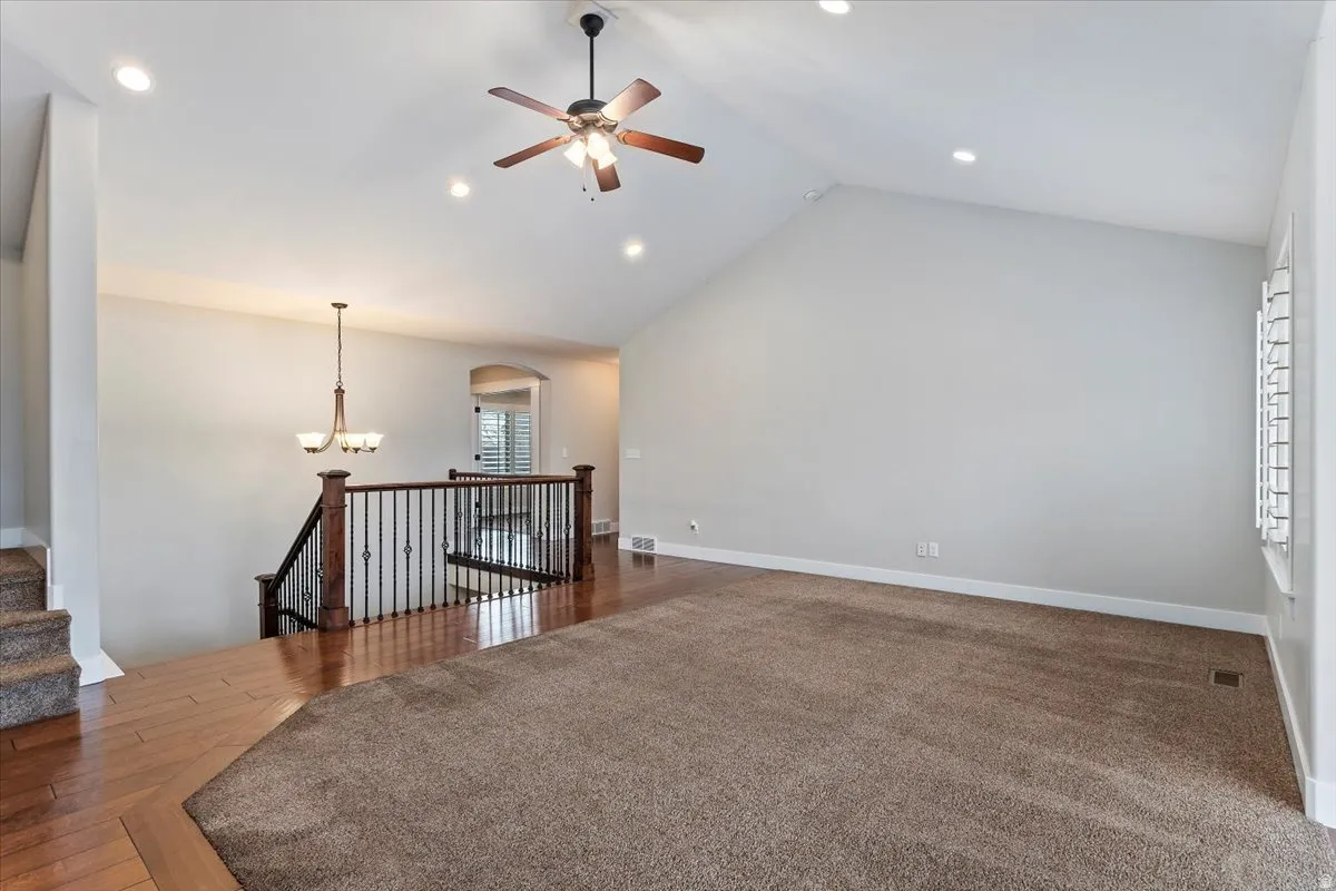 Unfurnished room with ceiling fan, a high ceiling, a chandelier, and dark wood-type flooring