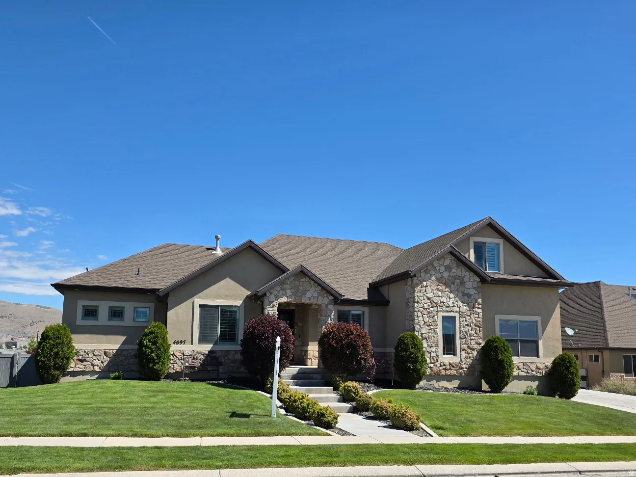 Exterior featuring stone and stucco facade, a prominent gabled dormer, and a well-maintained lawn with mature shrubbery