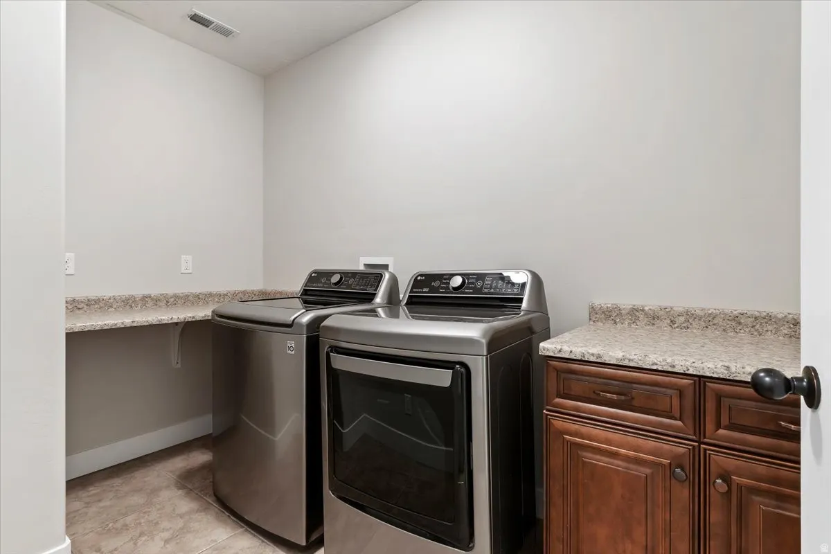 Laundry room featuring separate washer and dryer, light tile patterned flooring, and cabinet space