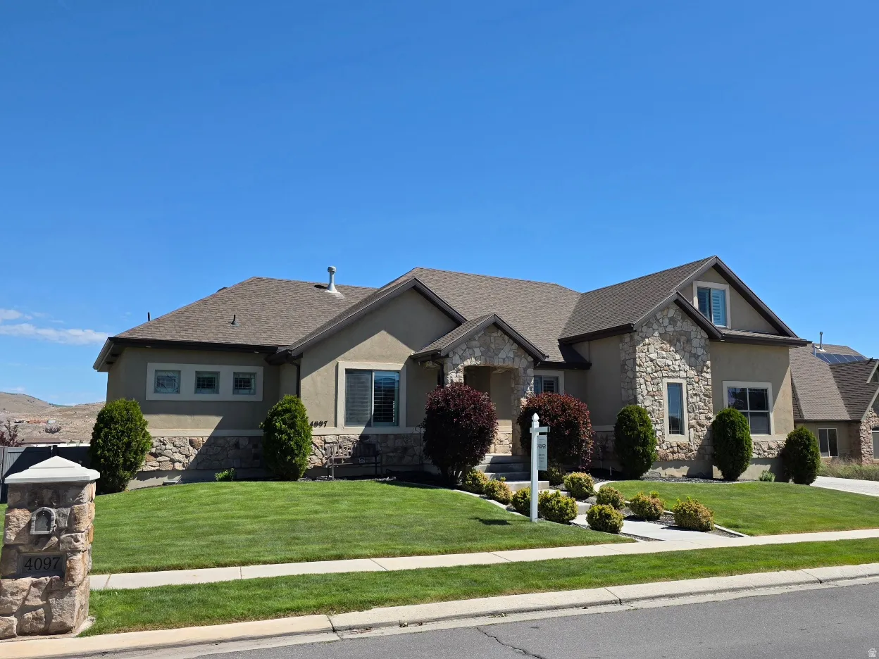 Stucco and stone exterior featuring a stone mailbox column, mature shrubbery, a manicured lawn, and a paved driveway