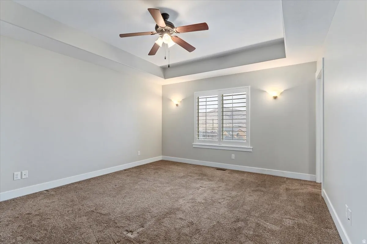 Carpeted empty room featuring ceiling fan and a tray ceiling