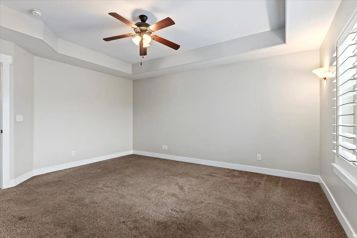 Empty room featuring a raised ceiling, dark colored carpet, and a ceiling fan