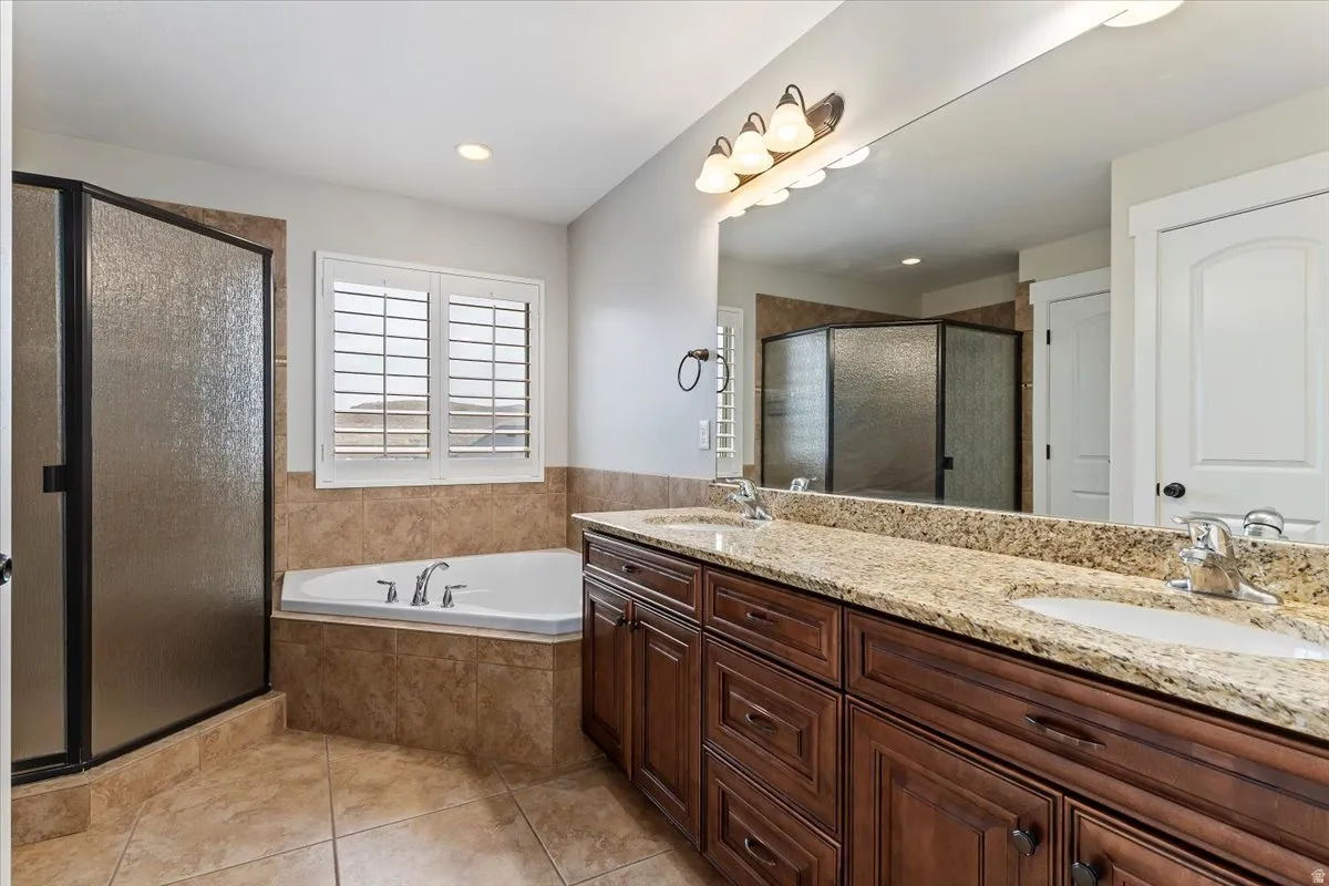 Full bath featuring double vanity, light tile patterned flooring, a garden tub, a stall shower, and recessed lighting