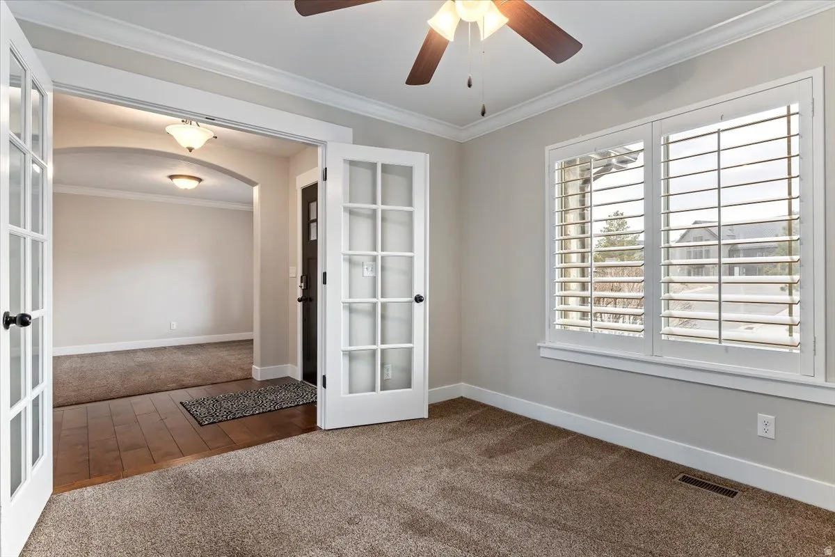 Spare room with arched walkways, dark carpet, crown molding, a ceiling fan, and french doors