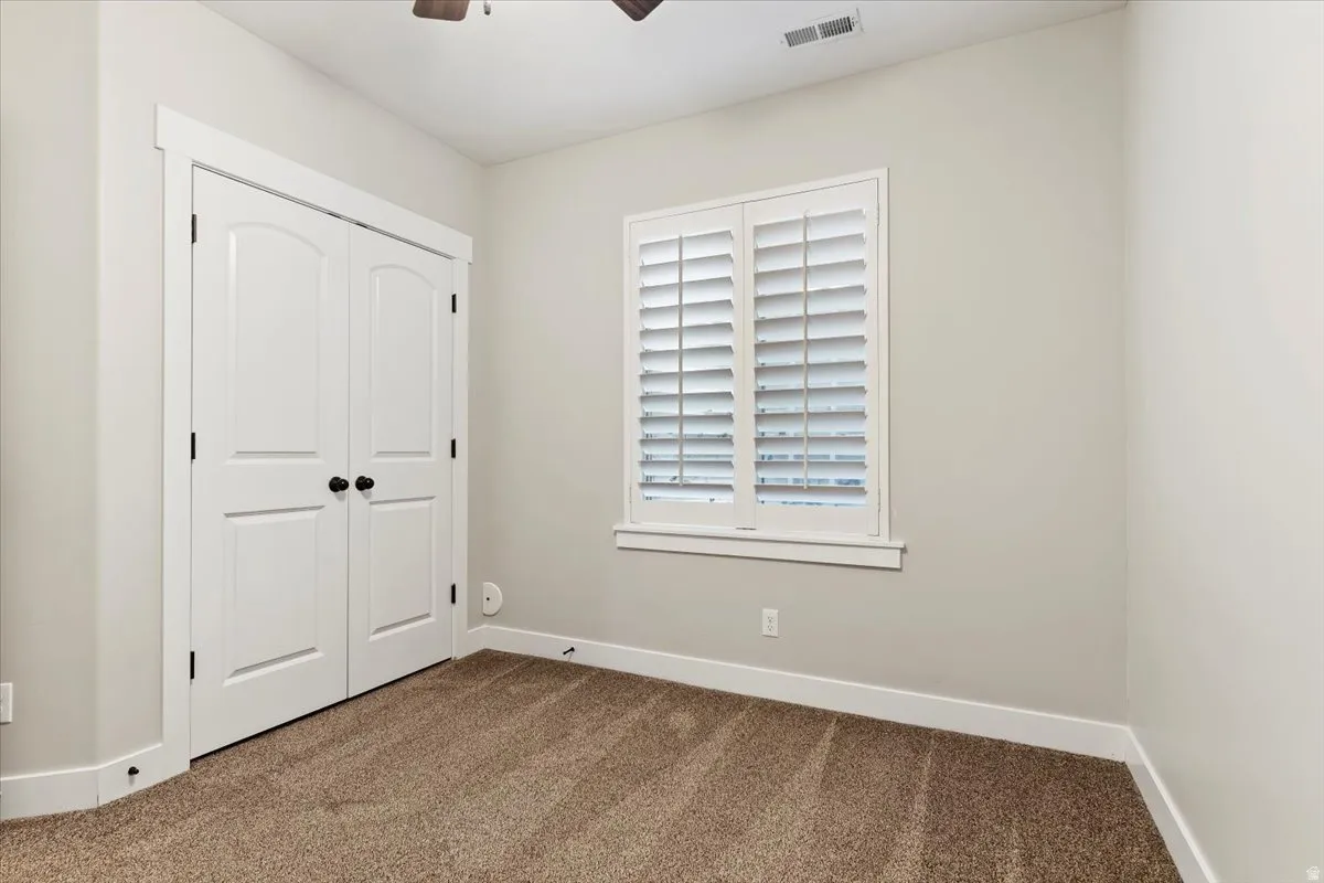 Unfurnished bedroom with dark colored carpet, a closet, and a ceiling fan