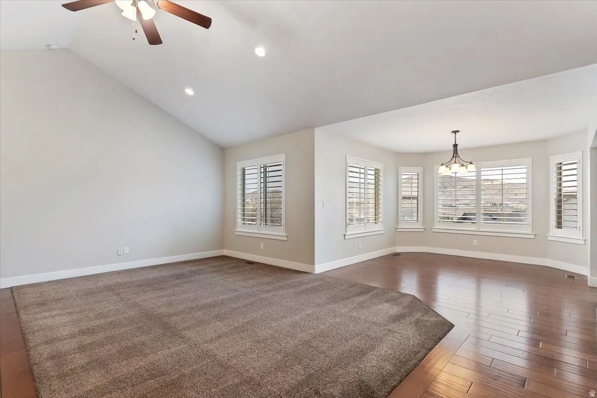 Unfurnished living room featuring ceiling fan, vaulted ceiling, hardwood / wood-style floors, and a chandelier