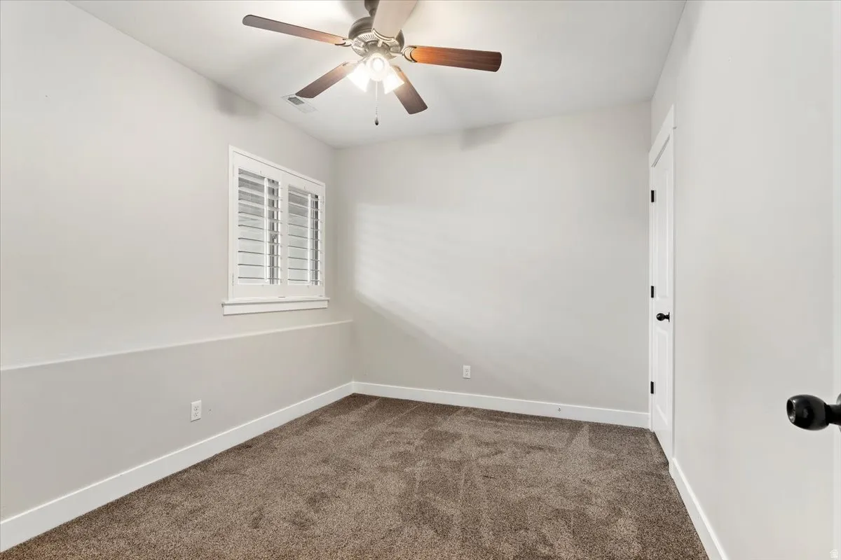 Unfurnished room featuring dark carpet and ceiling fan