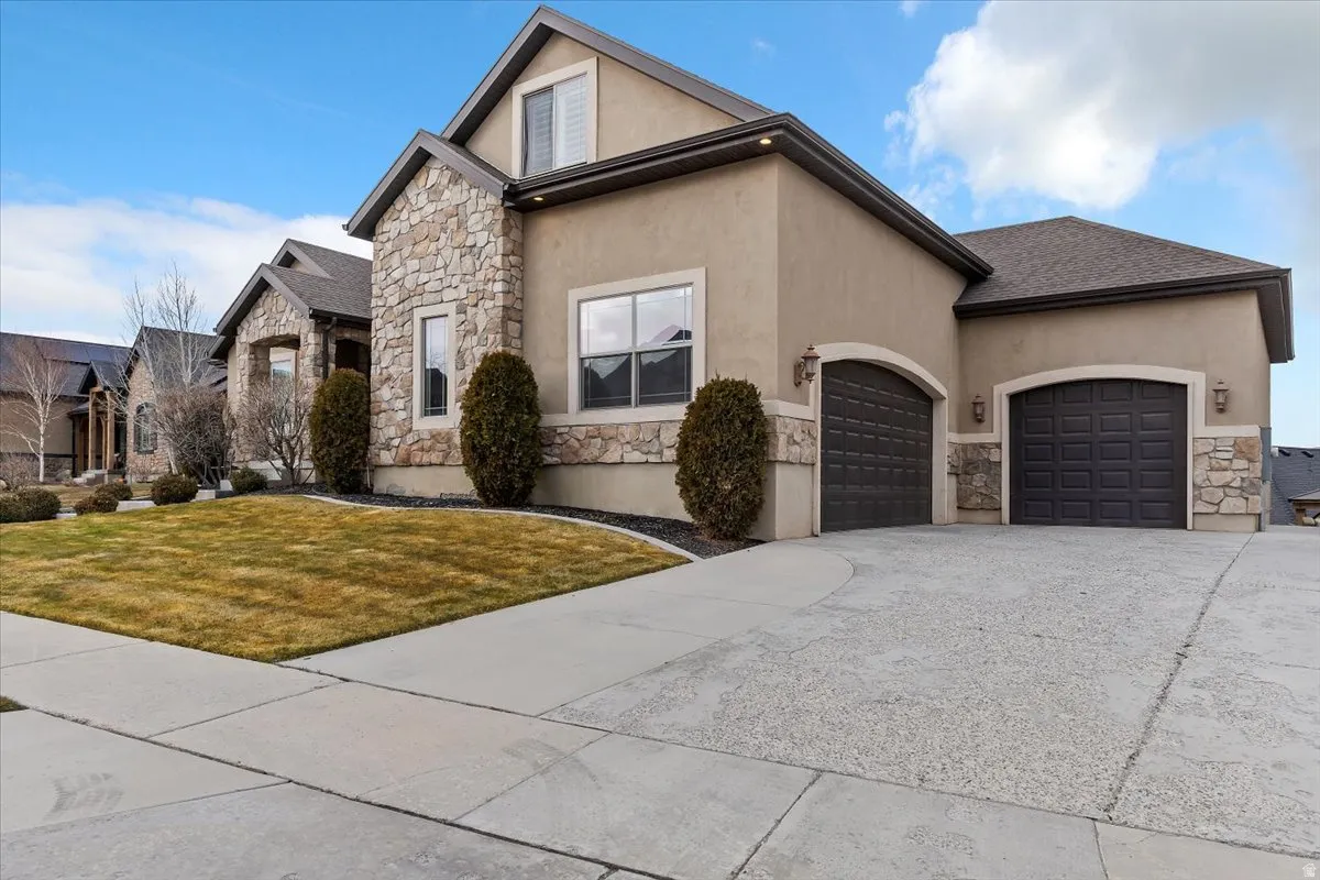 View of front of property with stone siding, an attached garage, concrete driveway, stucco siding, and a front yard