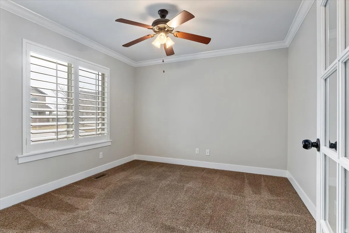 Empty room with dark carpet, crown molding, and ceiling fan