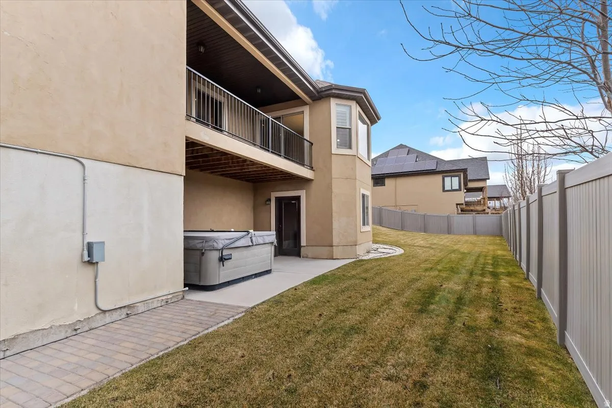 Rear view of property featuring stucco siding, a fenced backyard, a hot tub, a balcony, and a patio