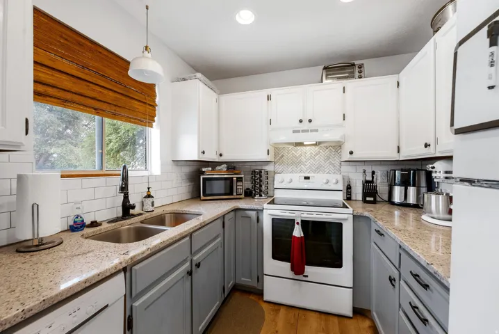 Kitchen featuring white appliances, decorative light fixtures, light stone counters, light wood finished floors, and dual tone cabinetry