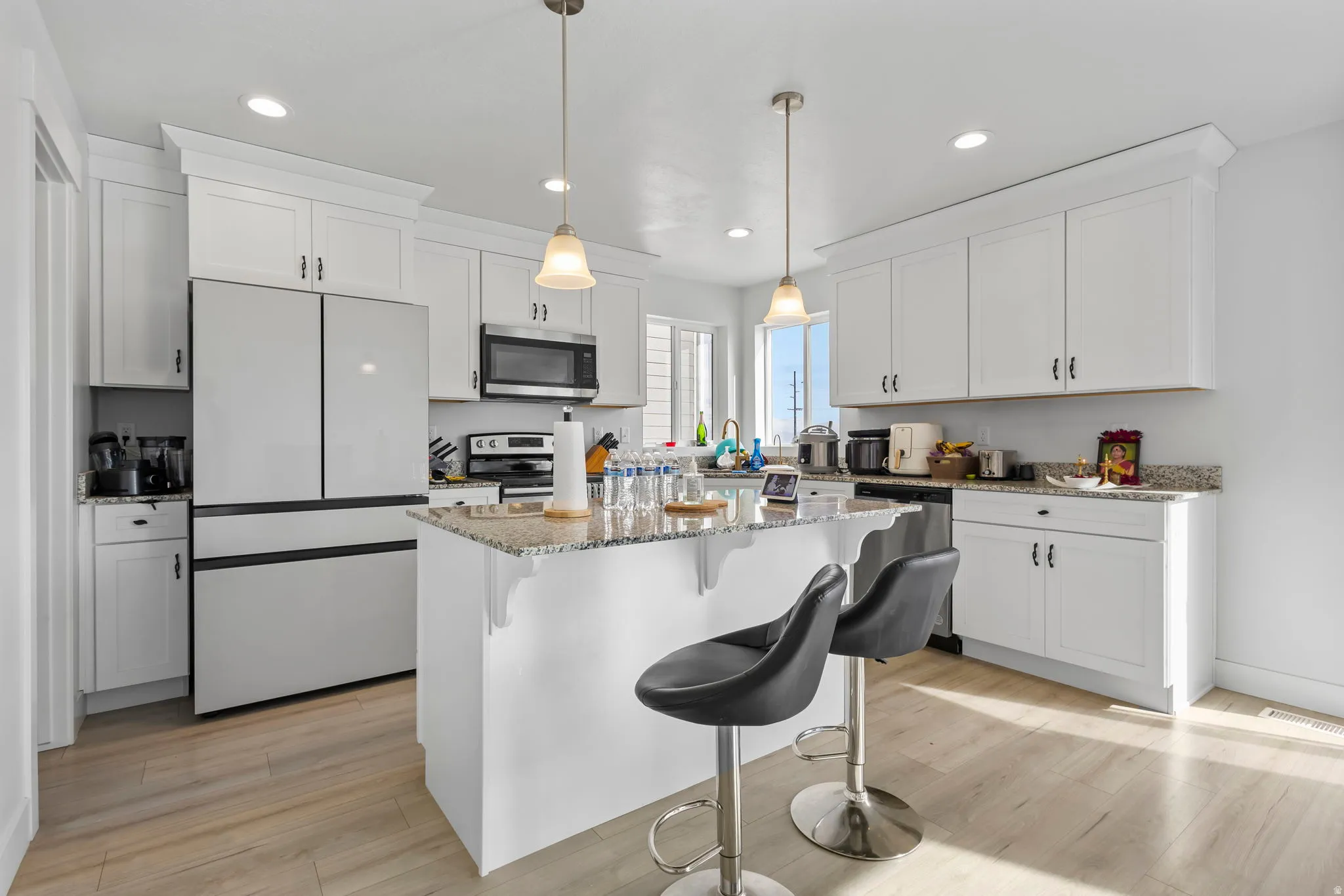 Kitchen featuring a breakfast bar area, stainless steel appliances, light stone counters, white cabinets, and decorative light fixtures