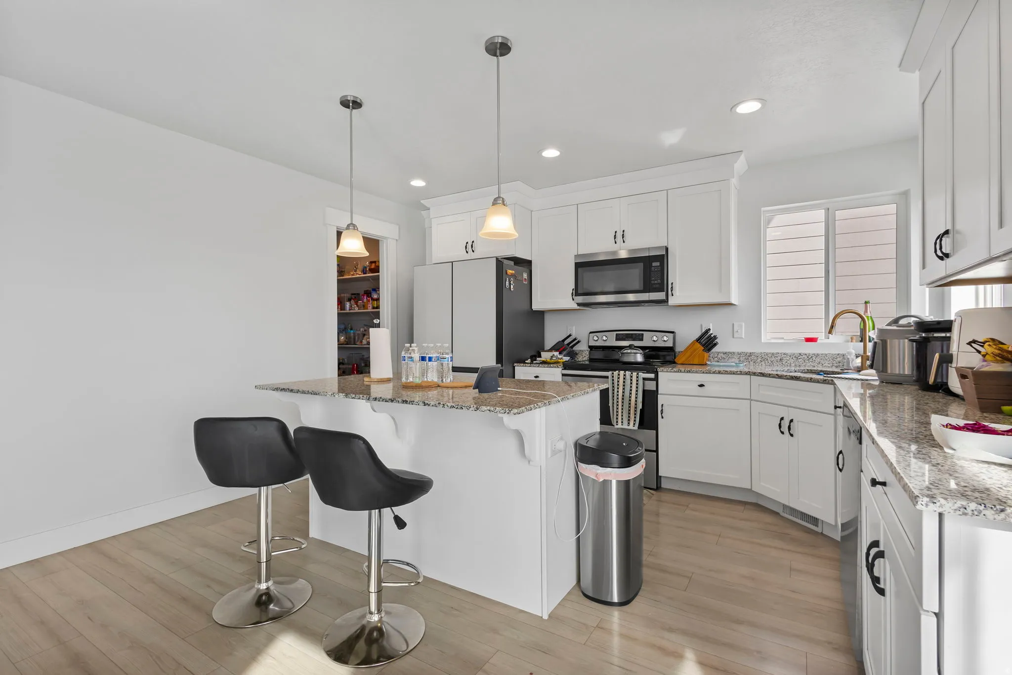 Kitchen featuring stainless steel appliances, light stone countertops, a breakfast bar, pendant lighting, and white cabinetry