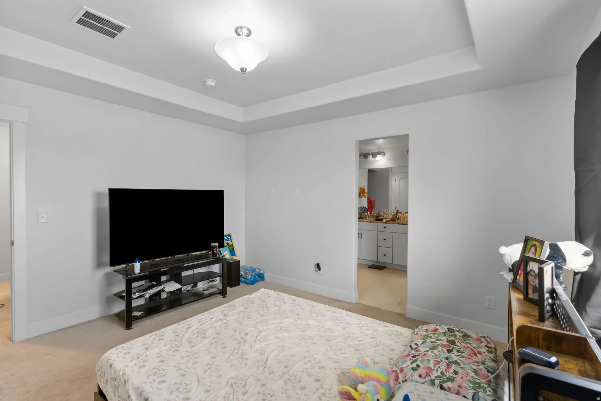 Bedroom featuring a raised ceiling, light colored carpet, and connected bathroom