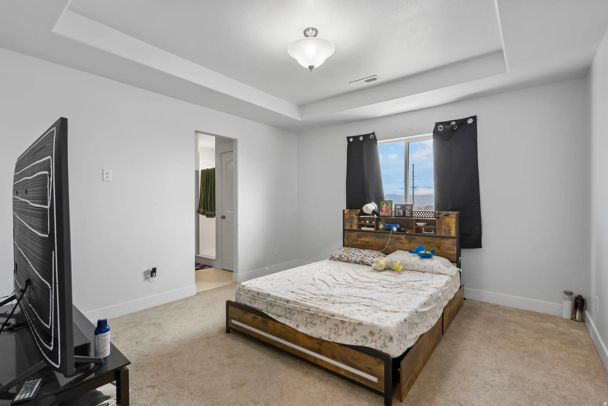 Bedroom with a tray ceiling, light carpet, and ensuite bath