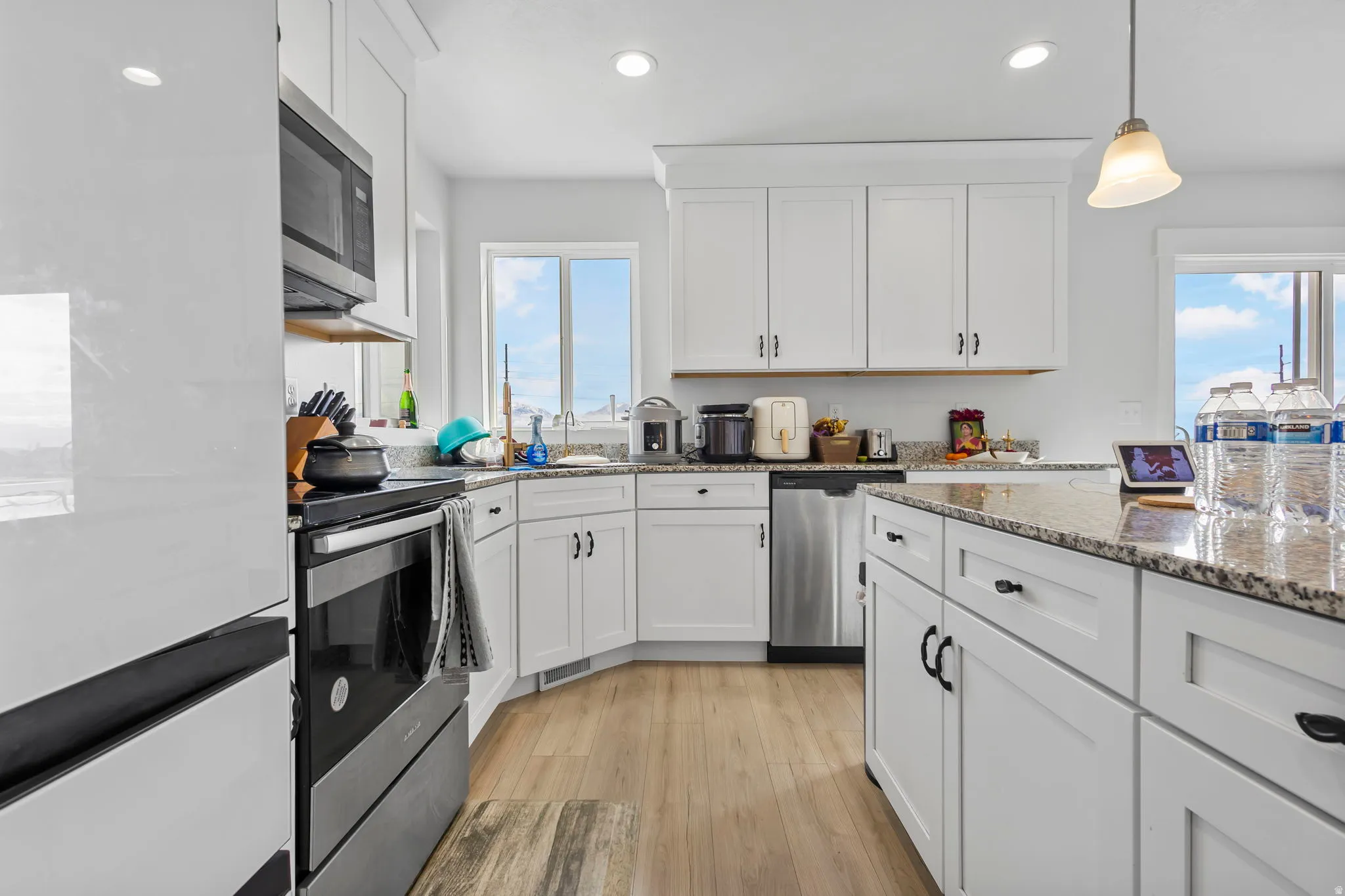 Kitchen with white cabinets, dark stone countertops, light wood-style flooring, hanging light fixtures, and stainless steel appliances