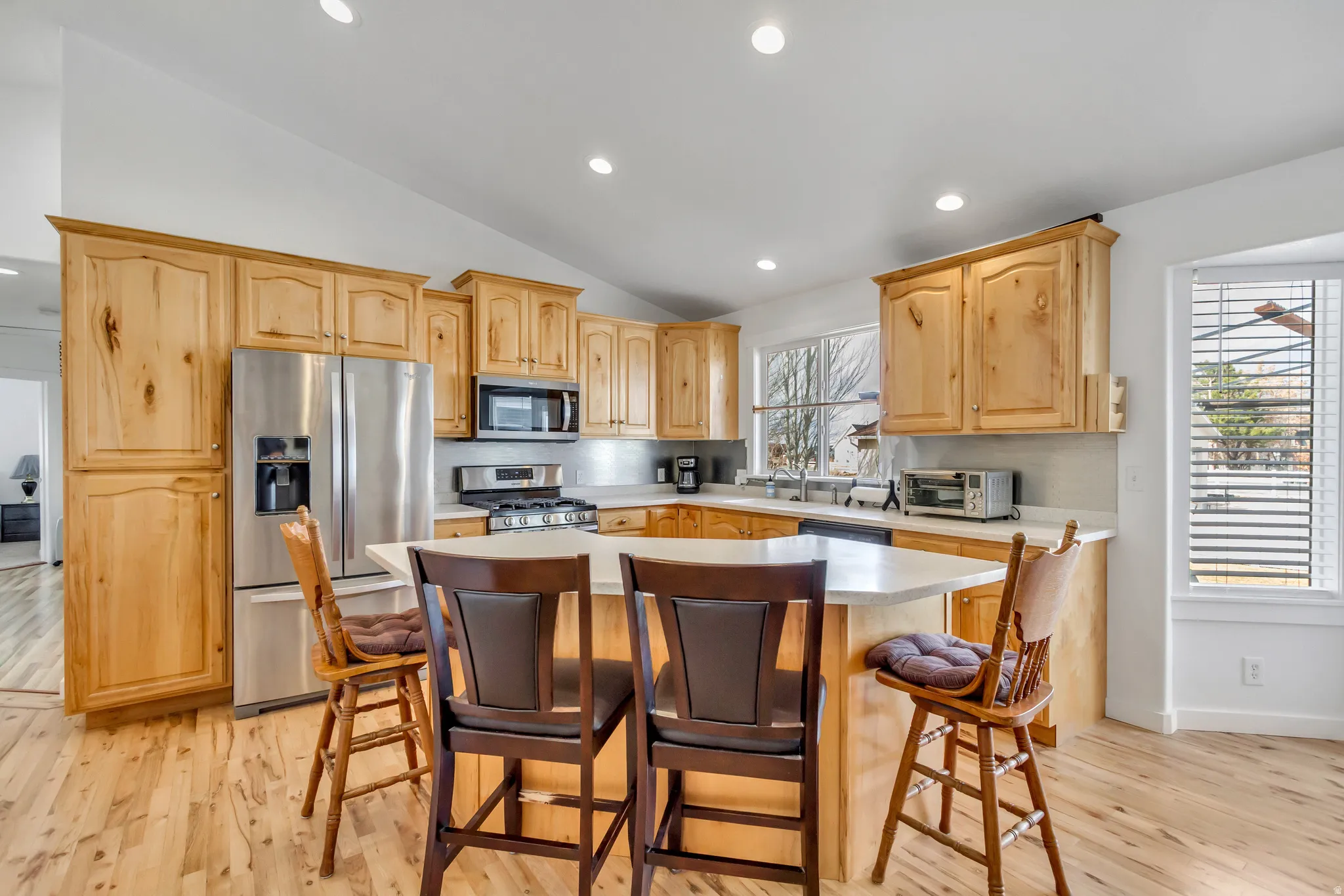 Kitchen featuring stainless steel appliances, light countertops, light wood finish cabinets, a breakfast bar area, and light wood-type flooring