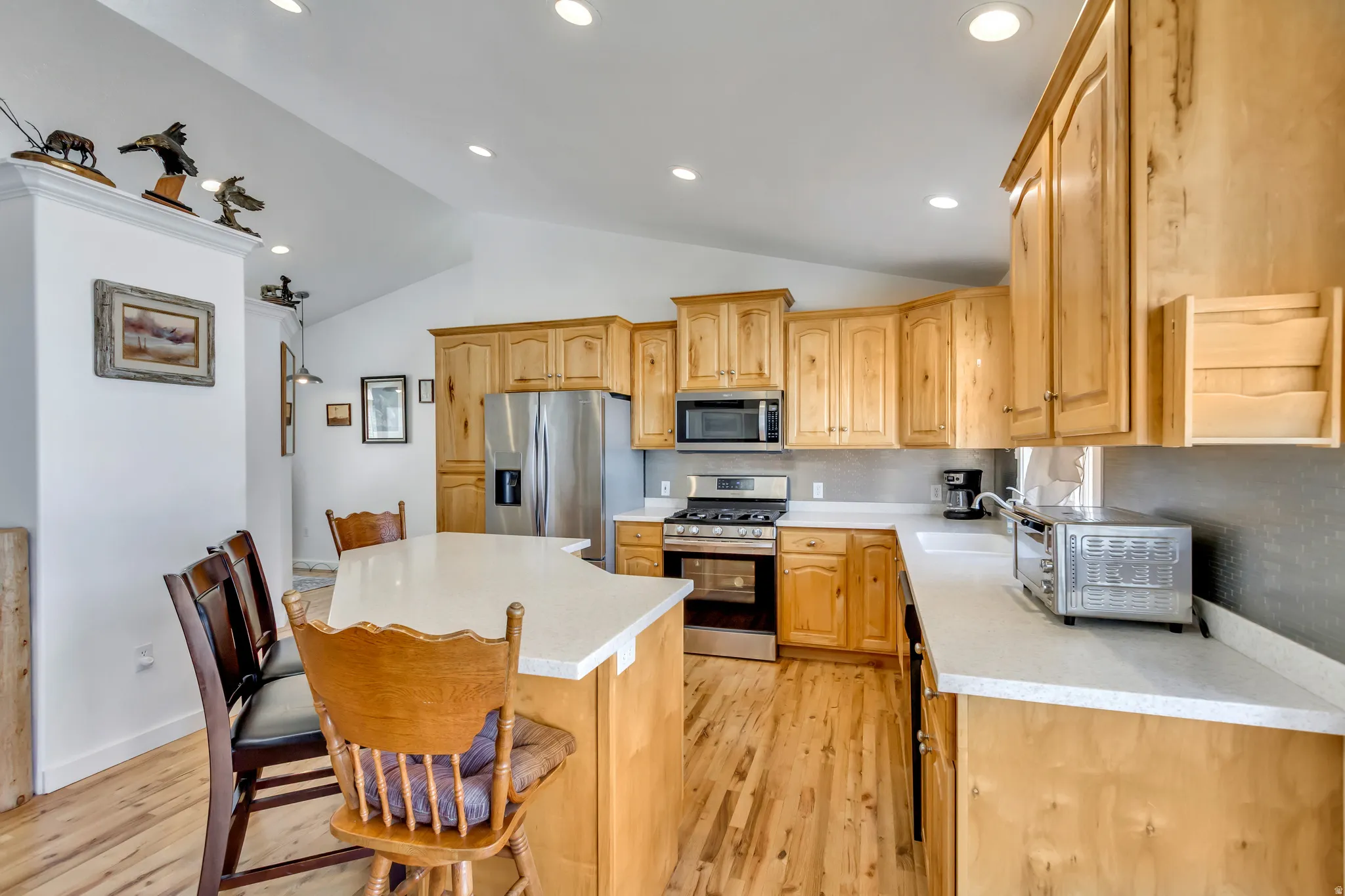 Kitchen with stainless steel appliances, a center island, lofted ceiling, light wood finish cabinets, and light wood-style floors