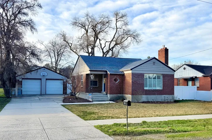Ranch-style house featuring an outbuilding, a detached garage, a chimney, brick siding, and a shingled roof